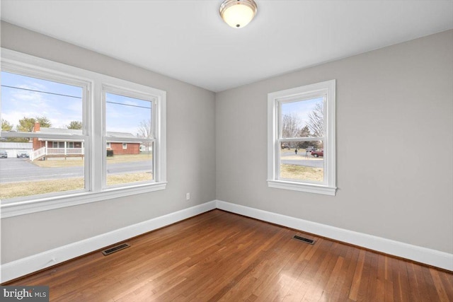 spare room featuring baseboards, visible vents, and wood finished floors