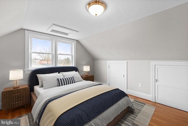 bedroom featuring lofted ceiling, baseboards, and wood finished floors