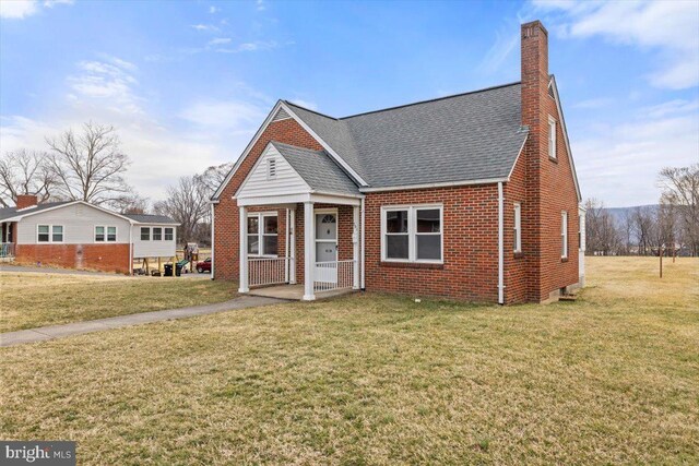 view of front of house featuring brick siding, a chimney, a shingled roof, a porch, and a front yard