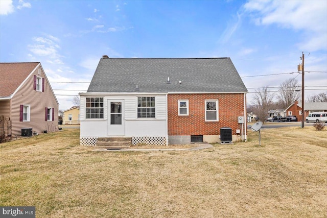 rear view of house with entry steps, a shingled roof, a lawn, central air condition unit, and brick siding