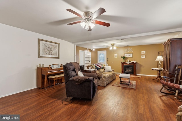 living area with ceiling fan, a glass covered fireplace, wood finished floors, and baseboards