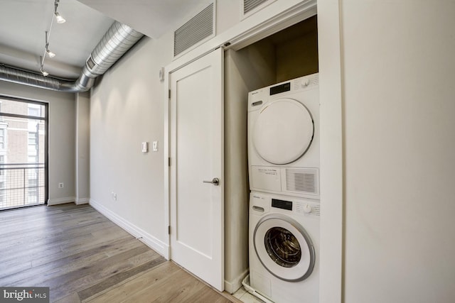 washroom featuring stacked washer and dryer, laundry area, visible vents, baseboards, and light wood-style floors