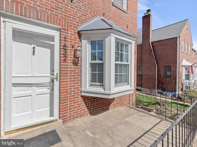 doorway to property featuring brick siding and fence