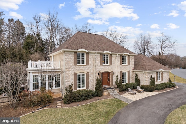 colonial inspired home featuring a shingled roof, brick siding, and a balcony