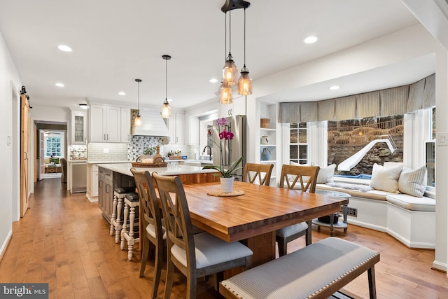 dining space featuring light wood finished floors, a barn door, baseboards, and recessed lighting