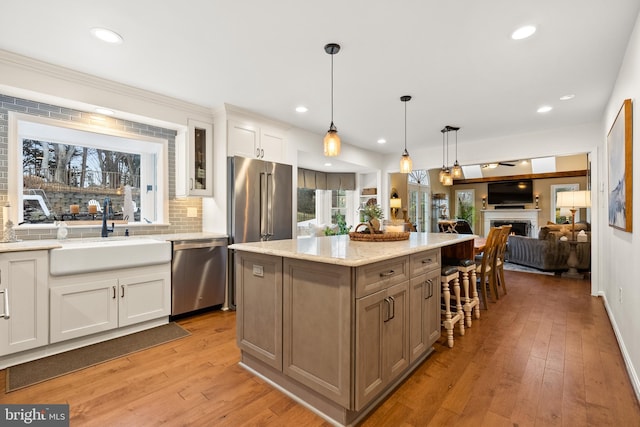 kitchen with a kitchen island, a sink, white cabinets, appliances with stainless steel finishes, and light wood-type flooring