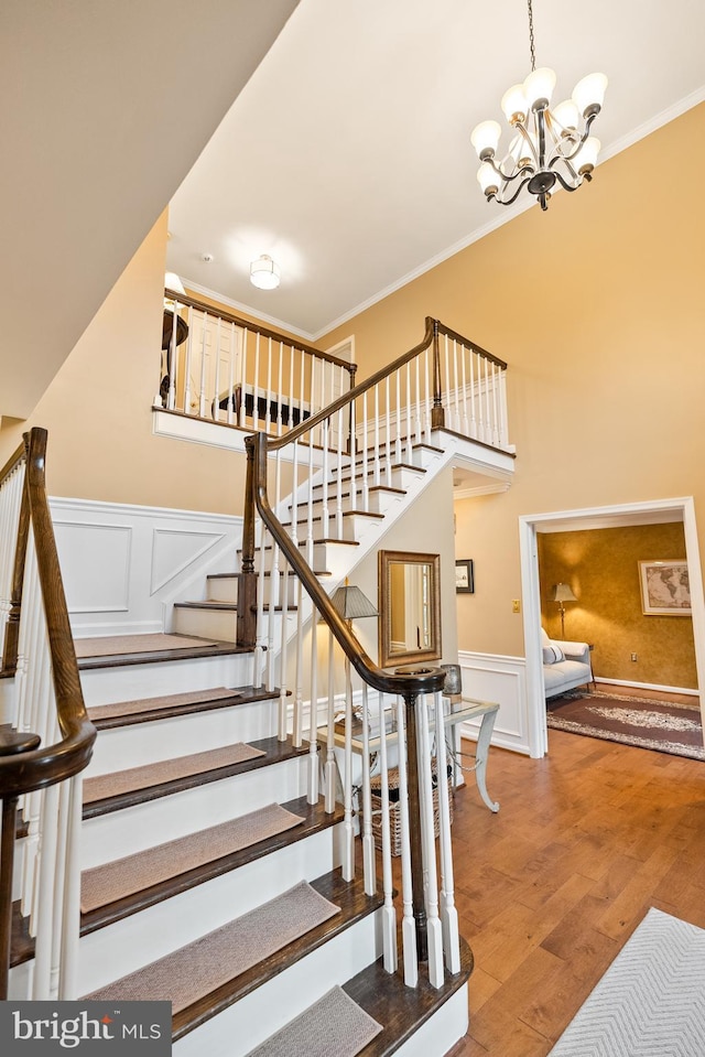 staircase with a decorative wall, an inviting chandelier, ornamental molding, wainscoting, and wood finished floors