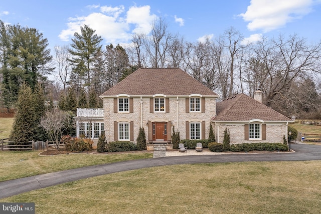 view of front of house featuring a shingled roof, a chimney, aphalt driveway, fence, and a front lawn