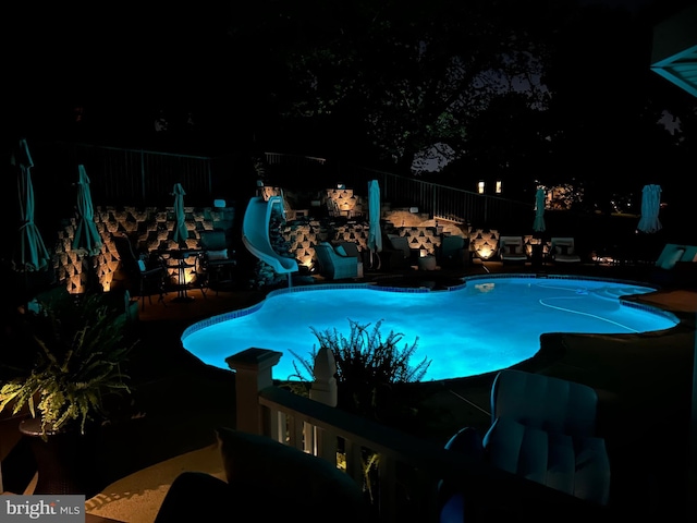 pool at twilight with an outdoor pool, a water slide, a patio area, and fence