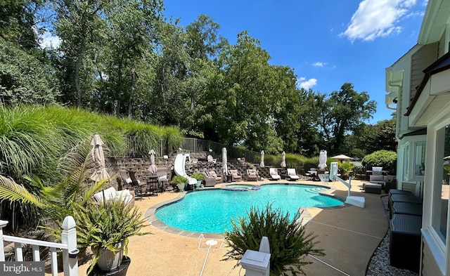 view of swimming pool with a water slide, a patio area, fence, and a pool with connected hot tub