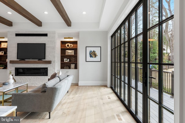 living area with built in shelves, beam ceiling, a fireplace, visible vents, and wood finished floors