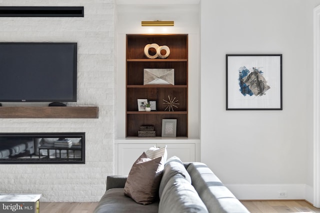 living area featuring built in features, a glass covered fireplace, baseboards, and wood finished floors