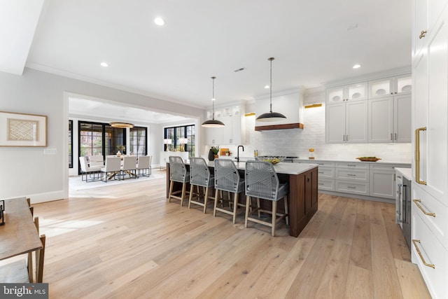 kitchen with light wood finished floors, light countertops, backsplash, an island with sink, and a kitchen breakfast bar