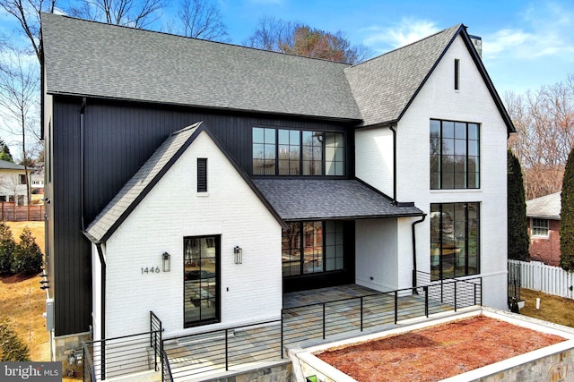 modern inspired farmhouse featuring roof with shingles, fence, and brick siding