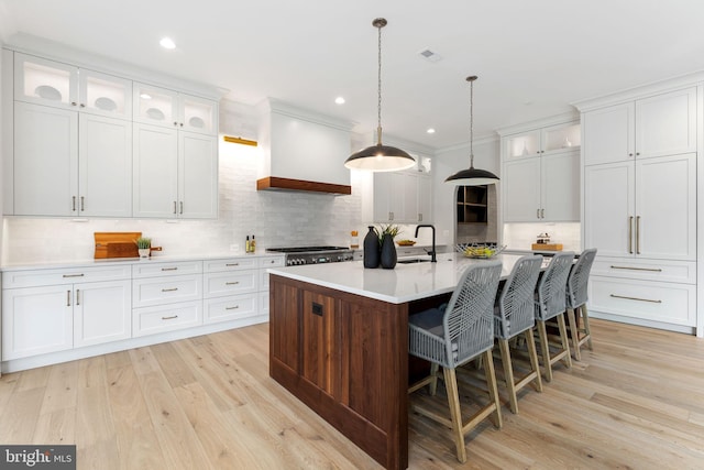 kitchen with a sink, light wood-style floors, light countertops, range, and custom range hood