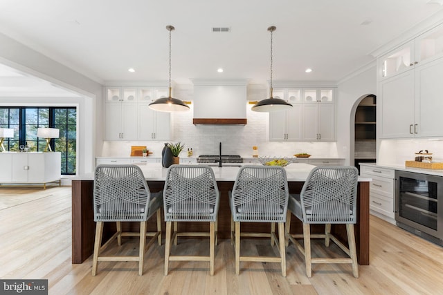 kitchen featuring beverage cooler, custom exhaust hood, light countertops, and arched walkways