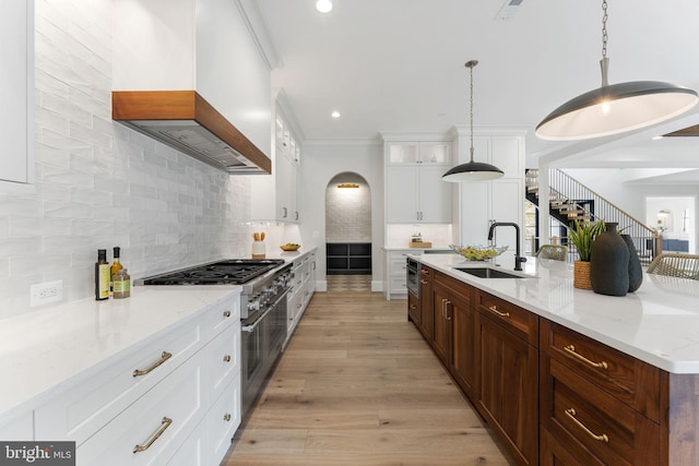 kitchen featuring light wood-style flooring, stainless steel stove, a sink, backsplash, and custom range hood