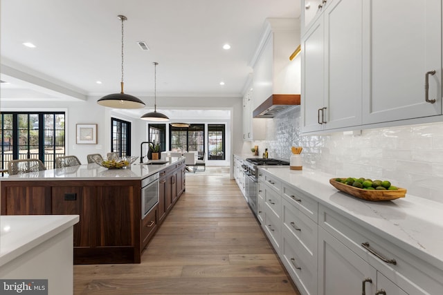 kitchen featuring high end stove, a sink, light wood-type flooring, tasteful backsplash, and custom range hood