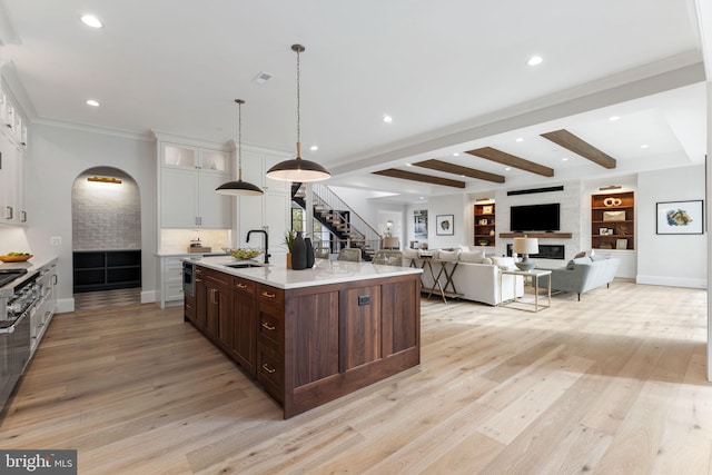 kitchen featuring arched walkways, light countertops, light wood-type flooring, white cabinetry, and beam ceiling