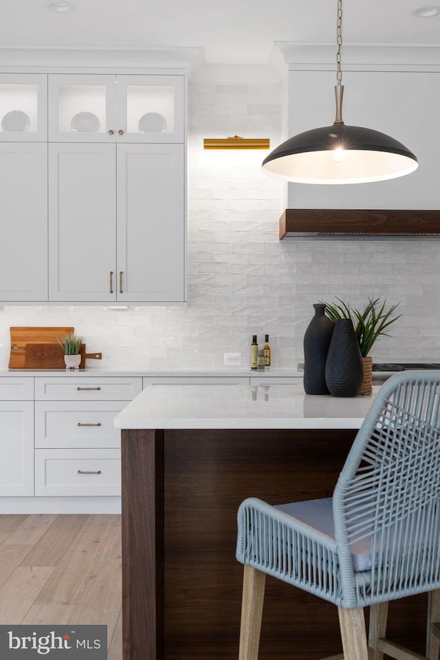 kitchen featuring light wood-style flooring, white cabinets, light countertops, decorative backsplash, and glass insert cabinets