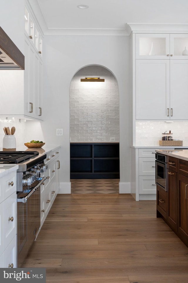 kitchen with crown molding, tasteful backsplash, custom range hood, glass insert cabinets, and wood finished floors