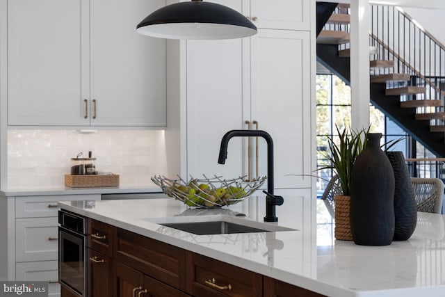 kitchen with light stone counters, dark brown cabinetry, a sink, white cabinets, and tasteful backsplash