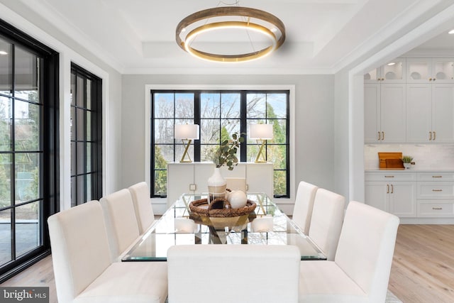 dining room with light wood-style floors, a raised ceiling, and crown molding