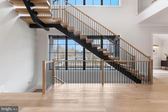 stairs with crown molding, a towering ceiling, baseboards, and wood finished floors