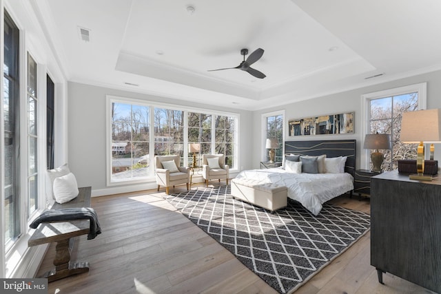 bedroom with wood-type flooring, a raised ceiling, and crown molding