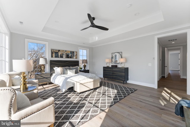 bedroom with a raised ceiling, visible vents, crown molding, and wood finished floors