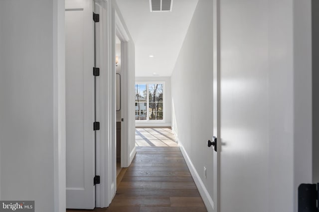 hallway with wood finished floors, visible vents, and baseboards