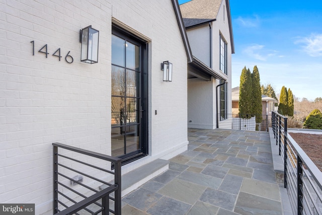 exterior space featuring brick siding and roof with shingles