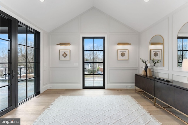 doorway to outside with vaulted ceiling, a decorative wall, and light wood finished floors