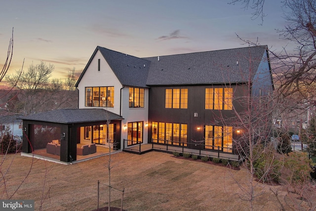 back of property at dusk with an outdoor living space, a patio, and roof with shingles