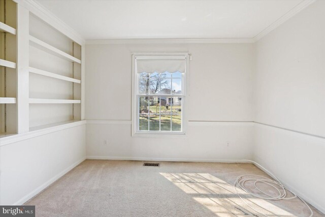 unfurnished room featuring visible vents, built in shelves, crown molding, baseboards, and carpet flooring