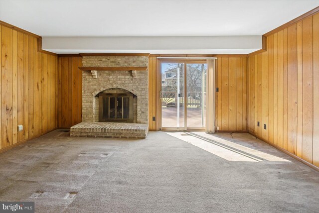 unfurnished living room with a brick fireplace, carpet flooring, and wood walls