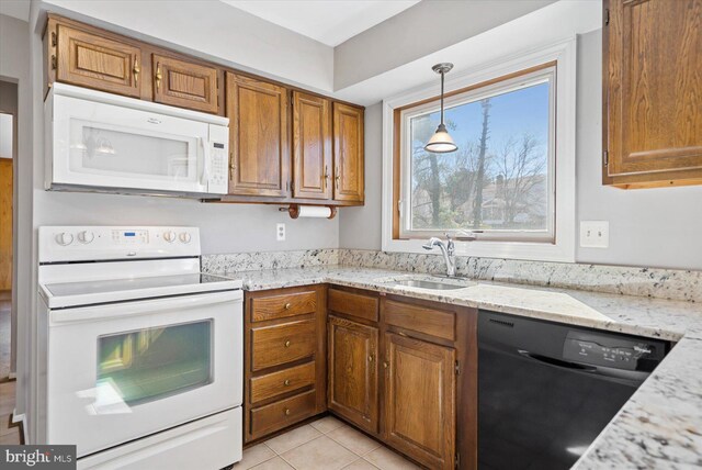 kitchen with brown cabinets, a sink, white appliances, light tile patterned floors, and light stone countertops