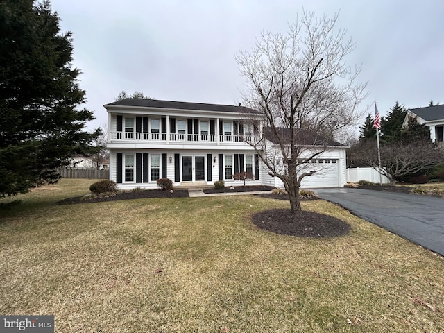 colonial-style house featuring a balcony, fence, driveway, a front lawn, and a garage