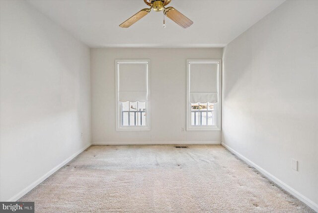 carpeted spare room with baseboards, visible vents, and ceiling fan