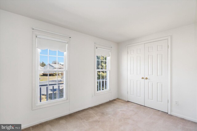 unfurnished bedroom featuring light carpet, baseboards, and a closet