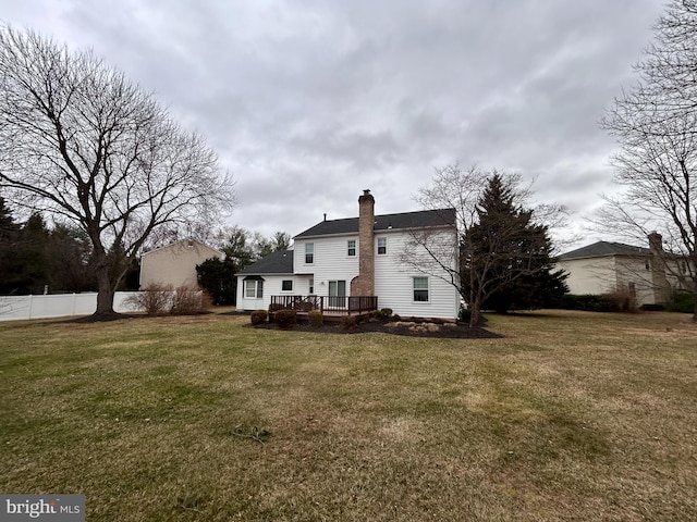 rear view of property with a lawn, a chimney, a deck, and fence