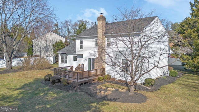 back of property with a wooden deck, a lawn, roof with shingles, and a chimney