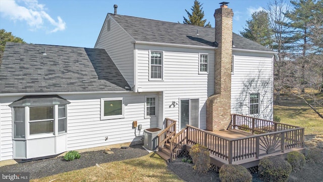 back of house featuring cooling unit, a chimney, a deck, and a shingled roof