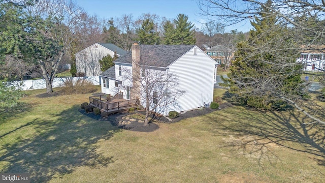 view of side of home featuring a lawn, roof with shingles, a deck, and a chimney