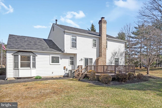 rear view of property with a deck, a yard, roof with shingles, central AC unit, and a chimney