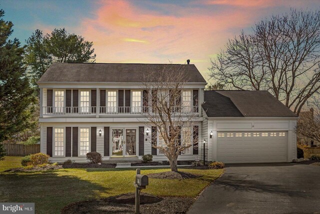 view of front facade with a balcony, fence, driveway, an attached garage, and a yard