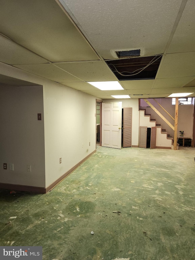 finished below grade area featuring stairway, baseboards, and a drop ceiling