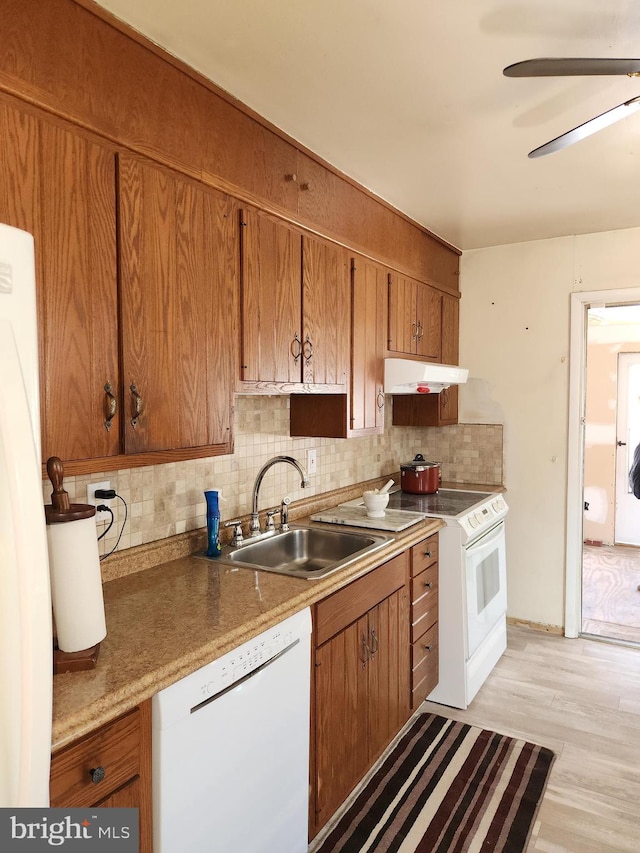 kitchen with under cabinet range hood, a sink, tasteful backsplash, white appliances, and brown cabinetry