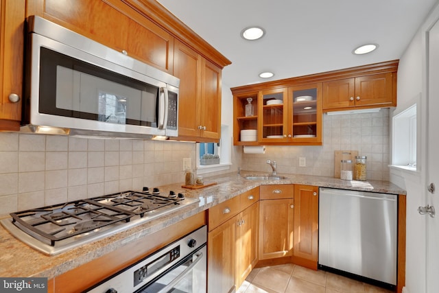 kitchen with brown cabinetry, light tile patterned floors, stainless steel appliances, and a sink