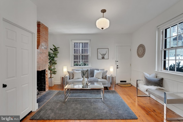 living area with a wainscoted wall, a brick fireplace, wood finished floors, and a decorative wall